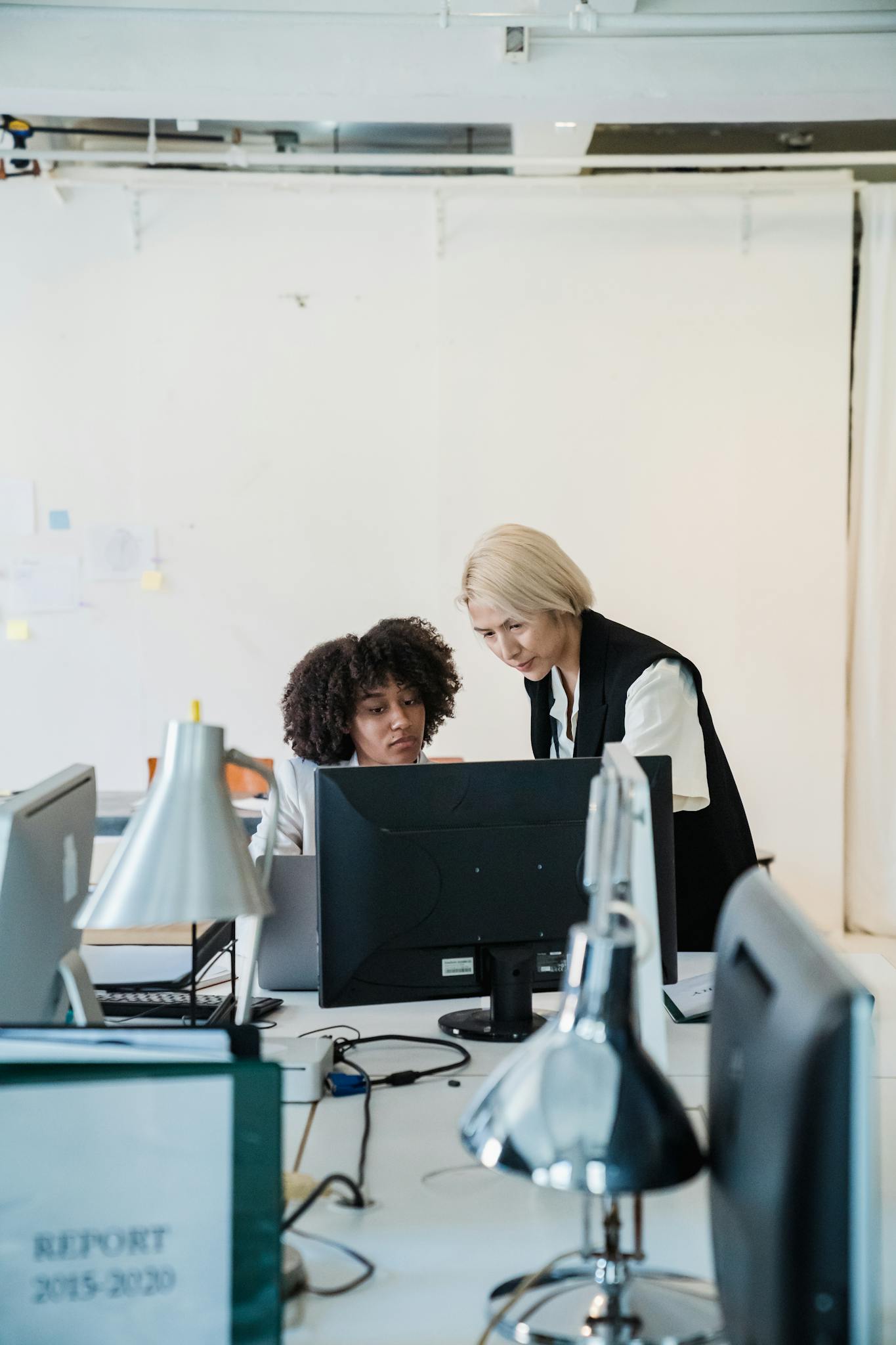 Two women collaborate on a project in a modern office setting, showcasing teamwork and diversity.