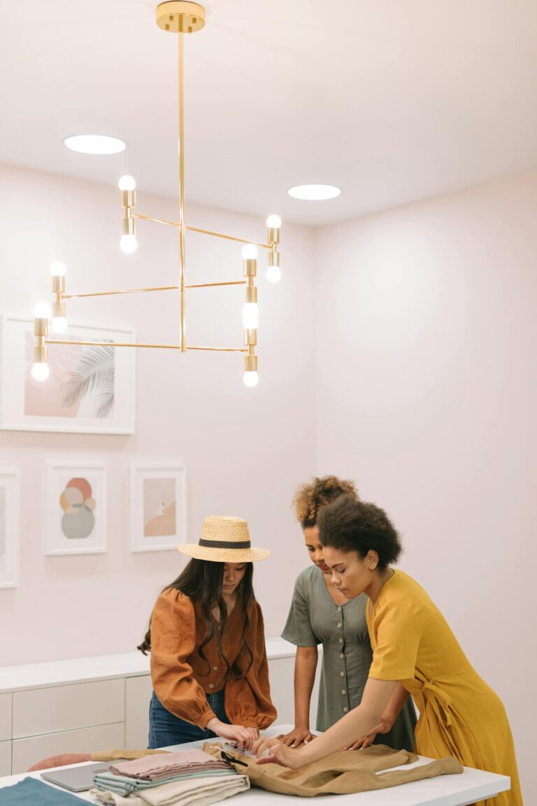 Three women in a modern office setting discuss fashion planning, showcasing teamwork and creativity.