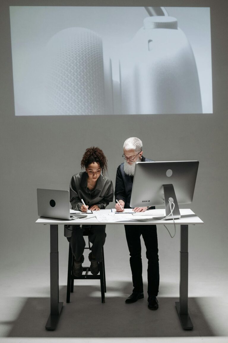 Two professionals collaborate in a high-tech setting with laptops and digital screens.